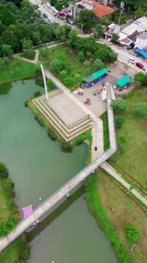 Nehir üzerinde köprüsü, yeşil manzarası ve insanları olan bir parkın insansız hava aracı görüntüleri. Tepeden çekim.