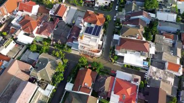 Güneş panelleri olan bir evin yüksek açılı insansız hava aracı görüntüsü. Çevredeki evler, sokaklar ve ağaçlar görülebilir..