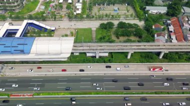 Bir Light Rail Transit (LRT) istasyonu, karayolu trafiği ve çevre şehir manzarasının yüksek açılı hava görüntüsü. Yumuşak kamera hareketi.