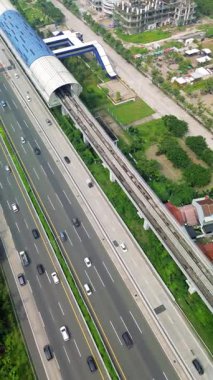 Light Rail Transit (LRT) istasyonunun yüksek açılı görüntüsü, hareket halindeki araçları ve çevre alanı olan otoyol. Yeşil alanlar ve görünen binalar.