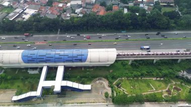 Bir Light Rail Transit (LRT) istasyonunun yüksek açılı görüntüsü, geçen tren, karayolu trafiği ve çevre kentsel manzara.