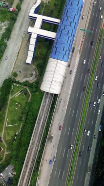 Light Rail Transit (LRT) istasyonu, tren yolu, hareket halindeki arabaları olan otoyol ve çevreleyen yeşillik manzarası. İnsansız hava aracı görüntüleri.