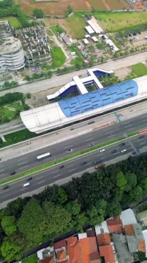 Bir Light Rail Transit (LRT) istasyonunun yüksek açılı görüntüsü, karayolu trafiği ve çevre şehir manzarası. Arabalar yol boyunca ilerliyor, ağaçlar ve binalar görünür..