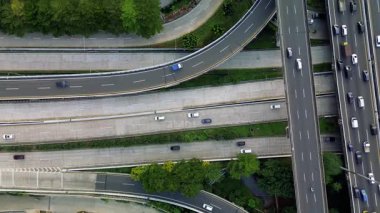 Yoğun trafik akışıyla karayolu kavşağının uzaktan kumandalı görüntüsü. Birden fazla şeritte hareket eden arabalar, görünür yeşil alanlar.
