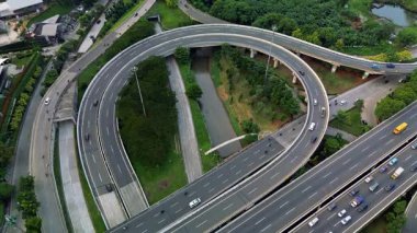 Yoğun bir otoyol kavşağının yüksek açılı görüntüsü bir drondan çekilen arabalar ve kamyonlarla. Yeşiller yolların etrafını sarmış..