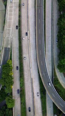 Karayolu trafiğinin insansız hava aracı görüntüsü. Arabalar çok şeritli yollarda sürerler. Otobanı çevreleyen yeşil ağaçlar.