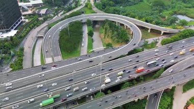 Yoğun bir otoyol kavşağının çeşitli araçlarla yüksek açılı görüntüsü. İnsansız hava aracı görüntüleri trafik akışını ve çevresindeki yeşillikleri gösteriyor.