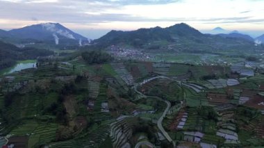 Bu hava görüntüleri, Endonezya 'nın yumuşak, erken bir sabah ışığı altında geniş bir pirinç tarlası, dolambaçlı bir yol, küçük bir göl ve görkemli dağları yakalar..