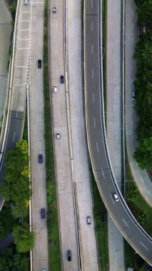 Karayolu trafiğinin insansız hava aracı görüntüsü. Arabalar çok şeritli yollarda sürerler. Otobanı çevreleyen yeşil ağaçlar.