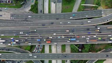Yoğun otoyol kesişiminin insansız hava aracı görüntüleri, çeşitli araçları ve trafik akışını gösteriyor. Yeşil alanlar görünür.