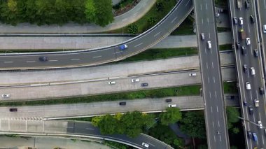 Yoğun trafik akışıyla karayolu kavşağının uzaktan kumandalı görüntüsü. Birden fazla şeritte hareket eden arabalar, görünür yeşil alanlar.