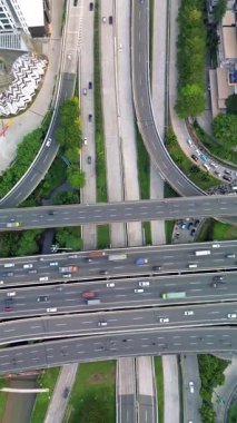 Yoğun bir şehir otobanının, arabalar ve kamyonlarla olan bir kavşağının insansız hava aracı görüntüleri. Yeşil alanlar görünür.