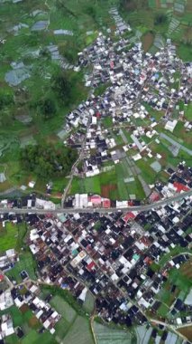 Hava görüntüleri, canlı yeşil pirinç terasları, dingin bir göl ve Endonezya 'nın kırsal kesiminde görkemli bir dağ arkaplanı arasında yuva yapmış bir köy yakalıyor. İHA atışı.
