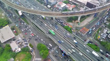 Havadan çekilen bir fotoğraf Jakarta otoyolunda trafik sıkışıklığını gösteriyor. Demiryolu köprüsünden bir tren geçiyor. Binalar ve yeşillikler işlek yolun etrafını sarar.