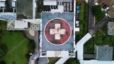 Bu görüntüler hastanenin tepeden tırnağa kızıl haçla işaretlenmiş helikopter pistini gösteriyor. Helikopter pisti binalar, yeşil çimenler, ağaçlar ve bir park alanı ile çevrili..