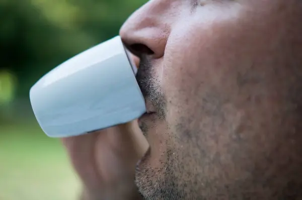 Genç adam yeşil çimlerin üzerindeki bir fincandan kahve içiyor..