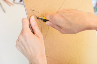 Öğretmen okula dönmek için karton maket bıçağıyla karton kesiyor.