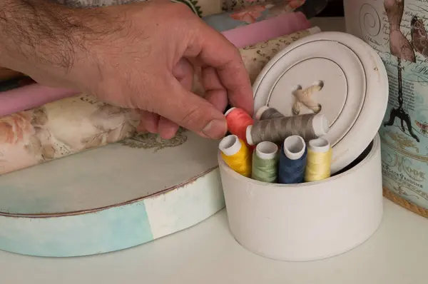 El dikiş makinesini tutuyor. Dikiş için renkli iplikler seti. Usta atölyede..