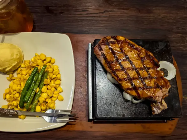 Demir tabakta barbekü soslu ızgara biftek, yanında patates püresi, mısır ve taze fasulye ile sağlıklı bir yemek..