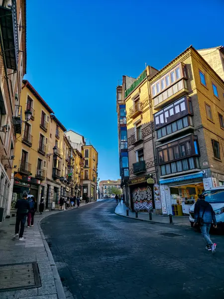 Toledo, İspanya 7 Nisan 2025: Toledo şehir merkezindeki tarihi binalar ve mağazaların kuşattığı eğimli bir caddede yürüyen turistler.