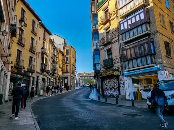 Toledo, İspanya 7 Nisan 2025: Bir grup insan Toledo 'nun tarihi merkezindeki taş binalarla çevrili dar bir alışveriş caddesinde yürüyor..
