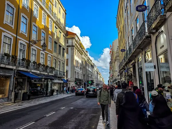 Lizbon, Portekiz 2 Nisan 2025: Lizbon şehir merkezinde eski binalar ve açık mavi gökyüzü altındaki dükkanlarla dolu bir cadde boyunca yürüyen kalabalık