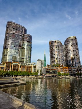 Perth, Avustralya 16 Haziran 2025: Çan Kulesi ve çevresindeki modern binalar Elizabeth Quay 'in sularında berrak bir öğleden sonra gökyüzü altında yansıdı..