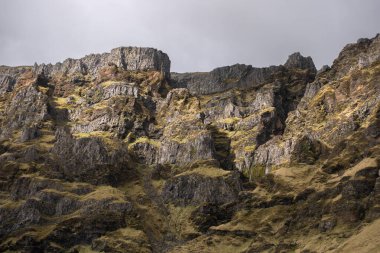 Görüntü dik, yıpranmış kaya oluşumları ve yosun kaplı yamaçlar gösteriyor, tipik dağlık arazi ya da bozkır ortamları. Uzak ve dokunulmamış doğanın mükemmel bir temsili. İzlanda