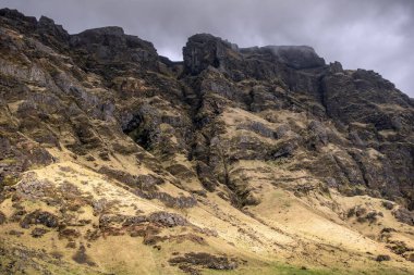 Katmanlı kaya katmanı ve canlı yeşil yosunlarla dağlık bir uçurumun çekilmesi bölgenin dramatik jeolojik tarihini vurguluyor. Jeoloji, seyahat ve doğa ile ilgili konular için ideal.