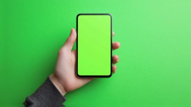 Elinde yeşil ekranlı bir cep telefonu var.