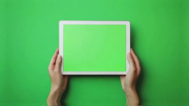 Yeşil arka planda boş ekranı olan tableti tutan kadın el kamerası, üst görünüm.