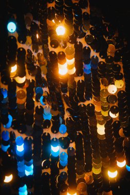 Pullu kumaşın bu yakın plan görüntüsü mavi ve kehribar ışıklarının yansıtıcı parıltısını yakalar. Katmanlı diskler parıltıyı dinamik, neredeyse ritmik bir şablonla yakalıyor. Çekime şenlikli ve rüya gibi bir atmosfer veriyor.