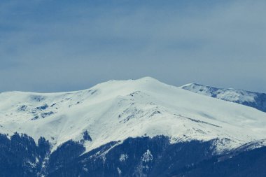 Snow Ridge Yakın Çekim - Karla kaplı bir dağ sırasının görünür bir dokusu ve yumuşak bir gökyüzüne karşı uzanan yumuşak yamaçlarıyla detaylı bir görüntüsü. Görüntü, kışların doğal formlarının saflığını ve minimalizmini vurguluyor..