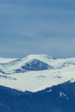  Karlı Tepeler - Yumuşak mavi bir gökyüzü altında geniş karla kaplı dağ sıralarının yer aldığı nefes kesici bir kış manzarası. Sahne, doğanın el değmemiş güzelliğini ve yüksek irtifadaki vahşi doğanın dingin gücünü yakalar..