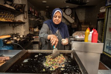 Kahire, Mısır. 30 Kasım 2022 'de Mısırlı bir kadın sıcak yeşil biber ve doğranmış ciğer kızartarak popüler bir Mısır sokak yemeği olan Kahire' de karaciğer sandviçi yapıyor.. 
