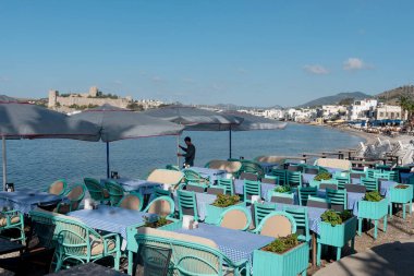 Bodrum, Mugla, Türkiye. 21 Nisan 2022 'de Bodrum limanındaki sahil tarafında masa hazırlayan bir garson arka planda Bodrum Şatosu, Türkiye' nin güneybatısındaki Ege kıyısı.  