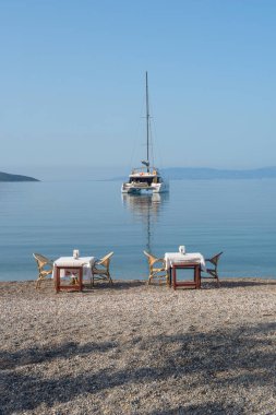 Bodrum, Mugla, Türkiye. 22 Nisan 2022 'de, Türkiye' nin güneybatısındaki Ege kıyısı boyunca popüler bir yelken ve gemi durağı olan Bodrum limanında demirlemiş bir Catamaran ile sahildeki restoran masaları.  