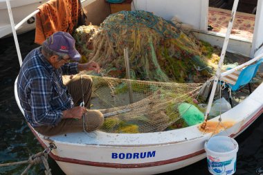 Bodrum, Mugla, Türkiye. 23 Nisan 2022 Bodrum kenti limanındaki teknesinde ağları onaran bir balıkçı, Türkiye 'deki Ege kıyı bölgesi popüler bir Türk turizm beldesi. 