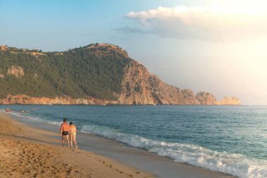 Türkiye 'nin Akdeniz kıyısındaki Türkiye tatil beldesi Alanya' da, gün batımında boş bir Kleopatra plajı boyunca yürüyen bir çift görülüyor.. 