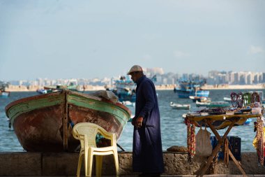 İskenderiye, Mısır. 1 Aralık 2022 'de Mısır' ın ikinci büyük kenti İskenderiye 'de Akdeniz kıyısındaki bir balıkçı teknesinin yanında resmi olmayan bir turistik hediyelik eşya standı.. 