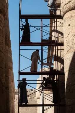 Luxor, Mısır. 12 Aralık 2022 'de Nil Nehri, Luxor, Yukarı Mısır yakınlarındaki Karnak Tapınağı' nın antik sütunlarını temizleyip restore eden yerel Mısırlı işçiler siluete katıldı..