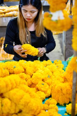 Bangkok, Tayland. 26 Mart 2025. Taylandlı bir kadın, Bangkok çiçek pazarı Pak khlong Talat 'ta geleneksel çiçek çelenkleri yapıyor..