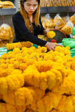 Bangkok, Tayland. 26 Mart 2025. Taylandlı bir kadın, Bangkok çiçek pazarı Pak khlong Talat 'ta geleneksel çiçek çelenkleri yapıyor..