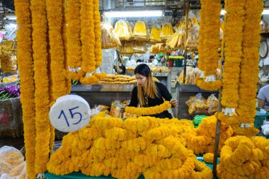Bangkok, Tayland. 26 Mart 2025. Taylandlı bir kadın, Bangkok çiçek pazarı Pak khlong Talat 'ta geleneksel çiçek çelenkleri yapıyor..