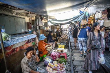 Mae Klong, Tayland. 15 Mart 2025. Turistler, Tayland 'daki Mae Klong Tren Marketi' nde taze yiyecek satan Tayland borsacılarıyla tren hatlarında dolaşıyorlar..