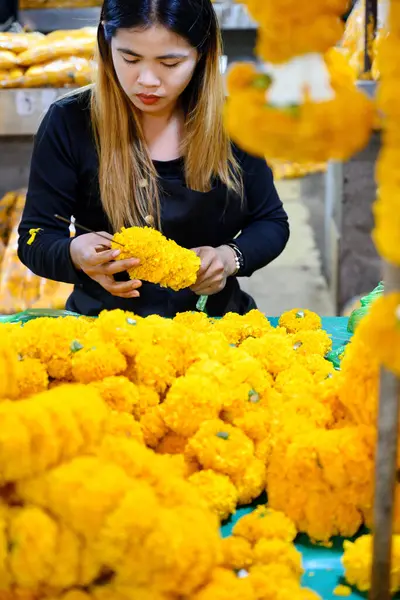 Bangkok, Tayland. 26 Mart 2025. Taylandlı bir kadın, Bangkok çiçek pazarı Pak khlong Talat 'ta geleneksel çiçek çelenkleri yapıyor..