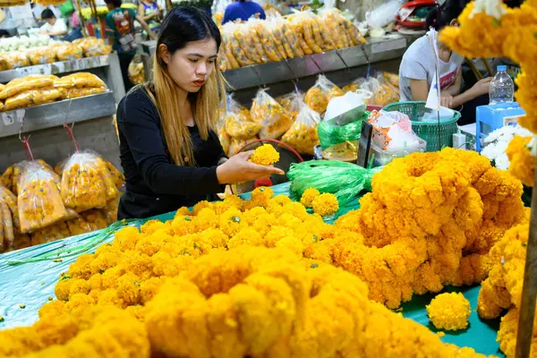 Bangkok, Tayland. 26 Mart 2025. Taylandlı bir kadın, Bangkok çiçek pazarı Pak khlong Talat 'ta geleneksel çiçek çelenkleri yapıyor..