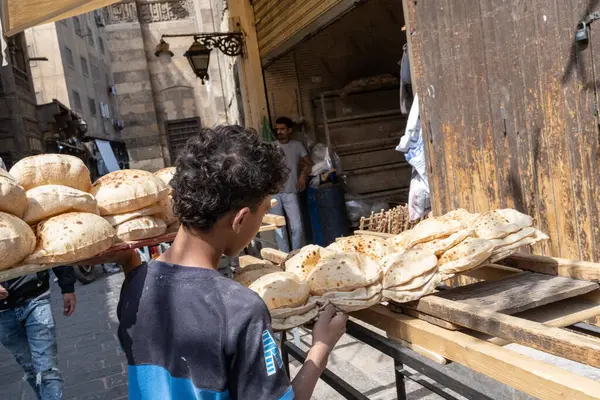 Kahire, Mısır. 15 Nisan 2025: Meşgul fırının önünde taze ekmek taşıyan çocuk