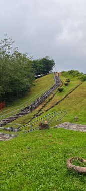 Önünde merdiven olan, yemyeşil tepelerden geçen Malezya otoyolunun yüksek manzarası. Seyahat, editör ve manzara görselleri için altyapı ve doğanın doğal karışımı.