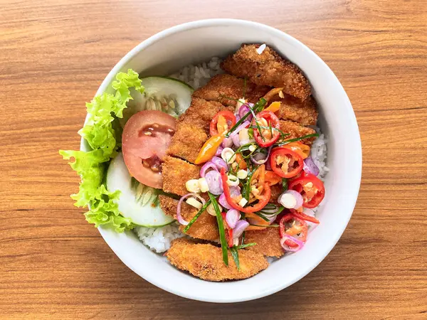 Pilav üzeri çıtır çıtır Katsu tavuğu, üzerinde canlı baharatlı acı biber sosu ve taze sebzeler. Lezzetli ve tatmin edici bir yemek..